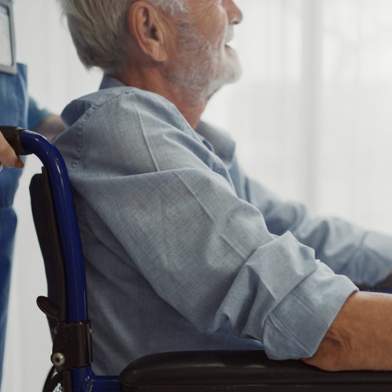 Stock_MannRollstuhl Nurse putting wheelchair with senior man window. Unhappy senior man having geriatric or depression disease. Therapist taking care, giving support and empathy.