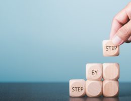 Hands arrange wooden blocks stacked into steps and display messages Step By Step. Business ideas for ladder of personal success, success and growth.
